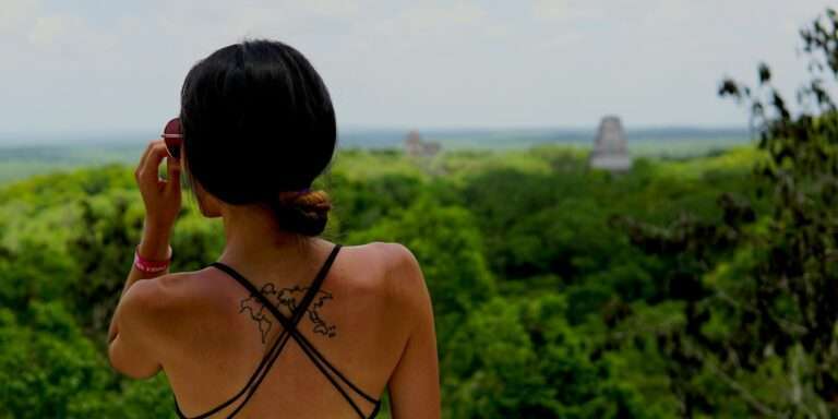 Femme vue de dos avec un tatouage de carte sur l'épaule, devant un paysage